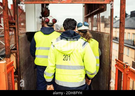 Rückansicht der Bauarbeiter, die im Aufzug vor Ort stehen Stockfoto