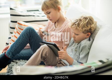 Geschwister, die mit Technologien zu Hause auf sofa Stockfoto