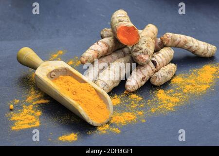 Kurkuma Pulver in einem Holzlöffel und Wurzeln auf einem dunklen Tisch (Curcuma longa), Kurkuma Stockfoto