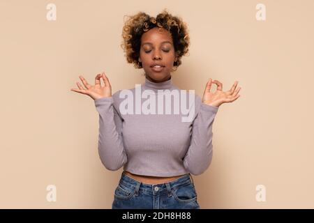 Junge afroamerikanische Frau, die sich entspannt und mit geschlossenen Augen lächelt und Meditationsgesten mit den Fingern macht. Yoga-Konzept. Stockfoto