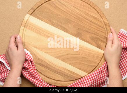 Frau mit leerem runden Holzpizzabrett in der Hand, Körper auf braunem Hintergrund, Draufsicht Stockfoto