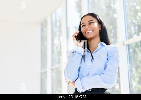 Lächelnde afroamerikanische Geschäftsfrau, die im offenen Raum telefoniert Modernes Büro Stockfoto