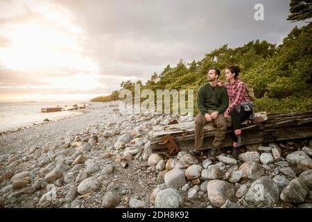 Pärchen sitzt auf Holz am Strand gegen Himmel Stockfoto