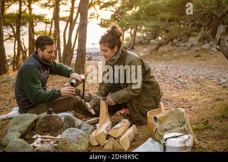 Mann Gießen trinken, während Frau mit Brennholz auf dem Campingplatz in Wald Stockfoto