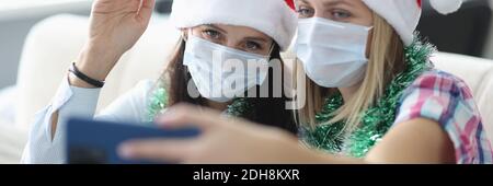 Zwei Frauen in Schutzmaske und weihnachtsmann Hut sprechen online am Telefon. Stockfoto