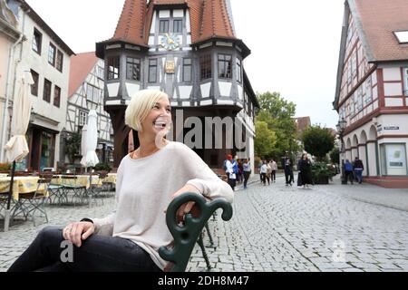 Junge Frau, die auf einer Bank sitzt und lächelt, mit dem Rathaus von Michelstadt im Hintergrund, Hessen, Deutschland. Stockfoto