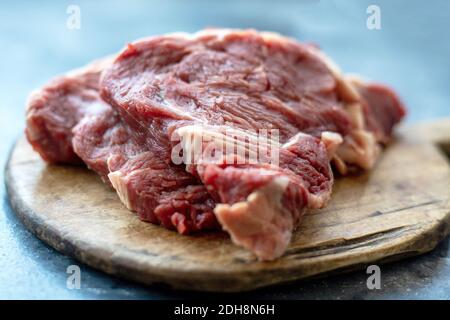 Rohes Fleischbeef Steak auf Holzschneidebrett auf bläulich schwarzem Hintergrund. Nahaufnahme. Selektiver Fokus Stockfoto