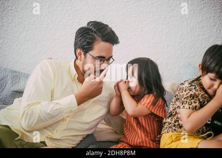 Lächelnder Vater unterrichtete Tochter, während er auf die Nase gegen die Wand zeigte Stockfoto
