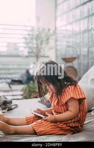 Down-Syndrom Mädchen mit digitalen Tablet, während auf dem Sofa sitzen Zu Hause Stockfoto