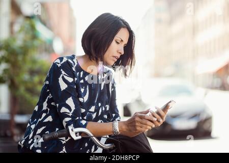 Geschäftsfrau mit Smartphone, während sie sich im Sommer auf dem Fahrrad lehnt Stockfoto
