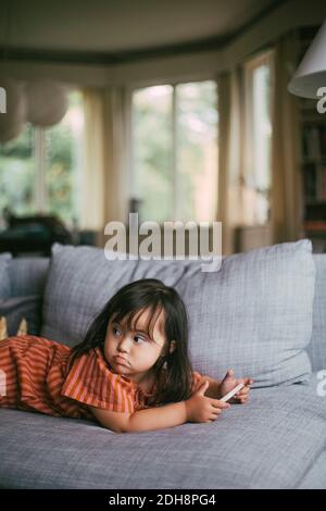 Down-Syndrom Mädchen suchen weg, während mit Smartphone auf Sofa zu Hause Stockfoto