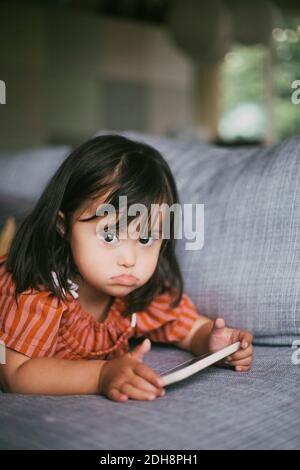 Portrait von Down-Syndrom Mädchen mit digitalen Tablet beim Liegen Auf dem Sofa zu Hause Stockfoto