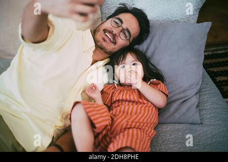 Lächelnder Vater nimmt Selfie mit Down-Syndrom-Tochter während liegend Auf dem Sofa zu Hause Stockfoto