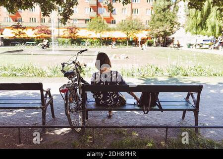 Rückansicht einer Geschäftsfrau, die mit dem Fahrrad auf der Parkbank sitzt Stockfoto