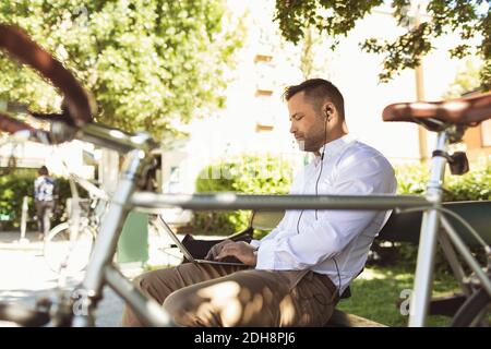 Seitenansicht des Geschäftsmannes, der auf dem Parkplatz sitzt und einen Laptop benutzt Bank Stockfoto