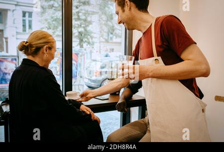 Lächelnde Besitzerin, die Kaffee und Wasser an weibliche Kundin gab Café Stockfoto