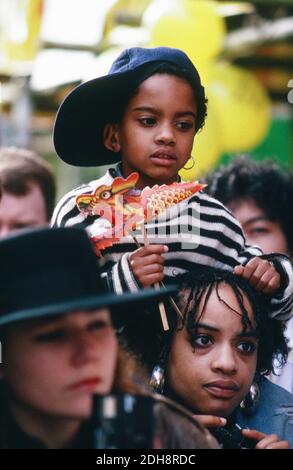 Ein kleines Kind beobachtet die Parade zum chinesischen Neujahrstag, wie es auf den Schultern seiner Mutter saß und einen Papierdrachen hielt. Chinatown, London. VEREINIGTES KÖNIGREICH Stockfoto