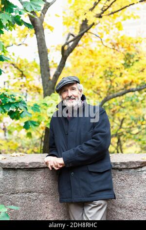 Porträt eines selbstbewussten älteren Mannes, der sich an der Stützmauer lehnt Stehen im Park im Herbst Stockfoto