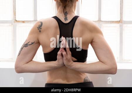 Rückansicht einer nicht erkennbaren Frau, die mit Namaste-Händen hinter dem Rücken steht und zu Hause Yoga macht. Stockfoto