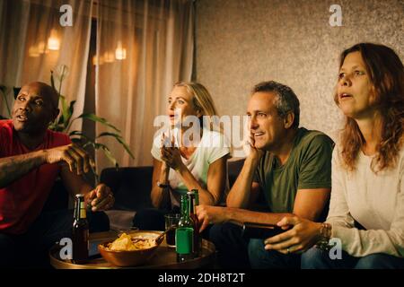 Heterosexuelle Paare beobachten Sport, während sie nachts auf dem Sofa sitzen Stockfoto