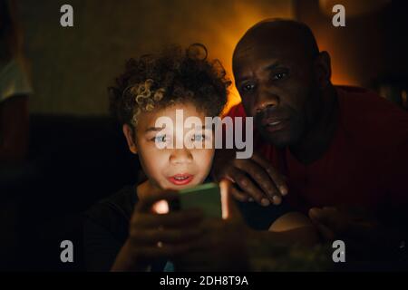 Junge mit Smartphone von Vater im Wohnzimmer bei Nacht Stockfoto