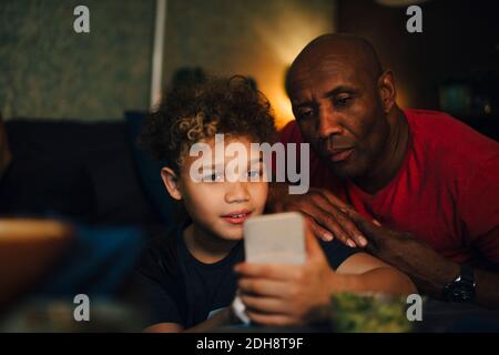 Junge mit Handy von Vater im Wohnzimmer bei Nacht Stockfoto