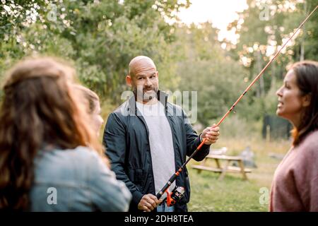 Vater mit Angelrute im Stehen mit Töchtern sprechen Partner im Hof Stockfoto