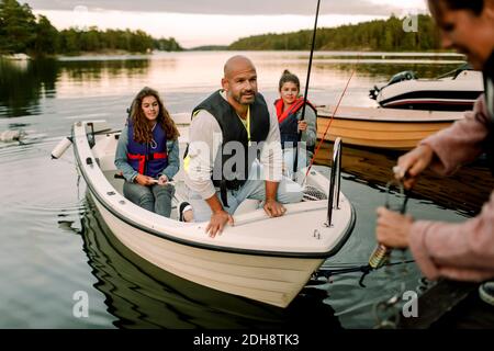 Familie schaut auf Frau, die Boot in der Nähe des Piers während des Sonnenuntergangs ankern Stockfoto