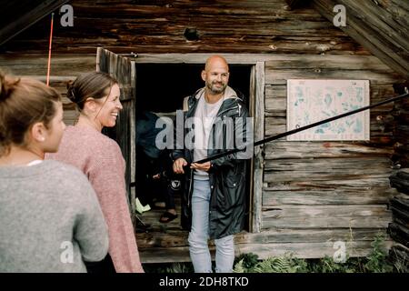 Lächelnder Vater hält Angelrute von Familie in der Nähe von Holzhaus Im Sommer Stockfoto