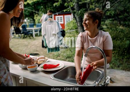 Lächelnde Tochter und Mutter sprechen während der Zubereitung von Essen im Hof Im Sommer Stockfoto