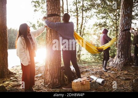 Männliche und weibliche Freunde hängen Hängematte im Wald während des Urlaubs Stockfoto
