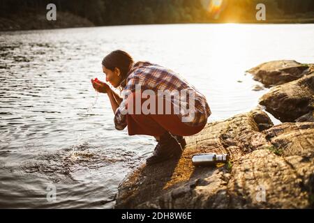 Seitenansicht der Frau, die Wasser aus dem See im Wald trinkt Stockfoto