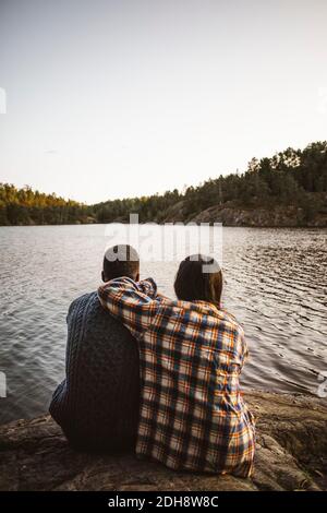 Rückansicht des Mannes und der Frau, die gegen den See sitzen Wald Stockfoto