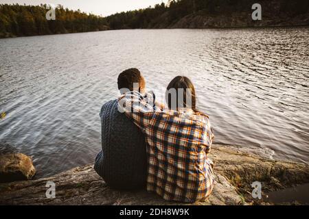 Rückansicht des Mannes und der Frau, die am See sitzen Wald Stockfoto