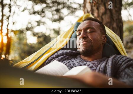 Mann mit Buch schläft in Hängematte im Wald Stockfoto