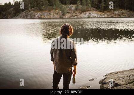 Rückansicht des jungen Mannes, der am See im Wald steht Während der Ferien Stockfoto