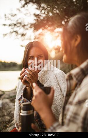 Lächelnde Freundinnen, die im Wald beim Kaffee trinken reden Stockfoto