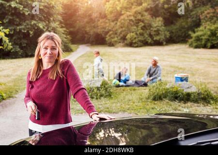 Porträt einer glücklichen Frau, die mit der Familie bei einem Elektroauto steht Im Hintergrund im Park Stockfoto