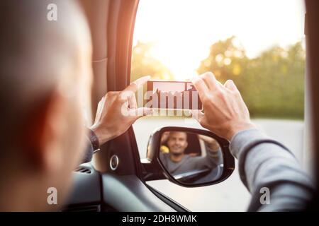 Rückansicht des Menschen beim Fotografieren vom Mobiltelefon mit Spiegelung Im Seitenspiegel Stockfoto