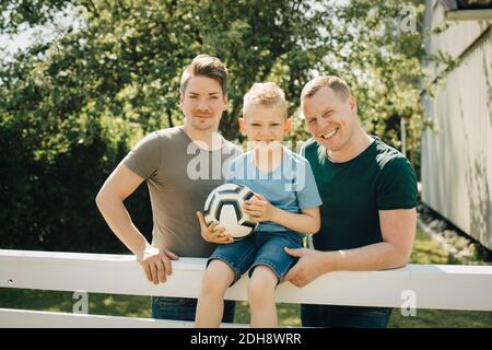 Porträt von homosexuellen Vätern mit Sohn hält Fußball in Hof Stockfoto