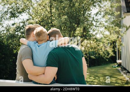Rückansicht des Sohnes mit Arm um Väter sitzen auf Zaun im Hof Stockfoto