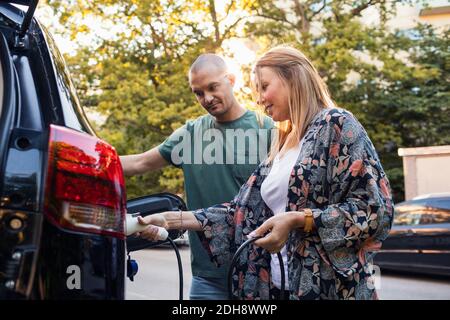 Reifes Paar lädt schwarzes Elektroauto im Hinterhof Stockfoto