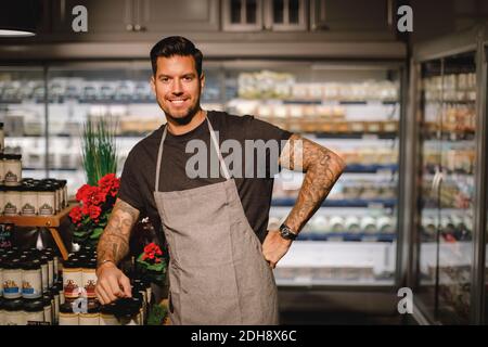 Porträt eines selbstbewussten Verkäufers mit Hand auf Hüfte im Lebensmittelgeschäft Speichern Stockfoto