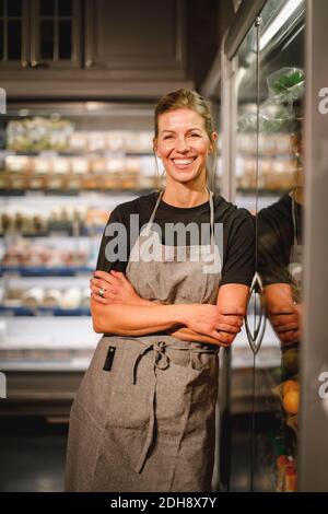 Porträt einer lächelnden Verkäuferin mit gekreuzten Armen, die sich über den Kühlschrank lehnen Im Supermarkt Stockfoto