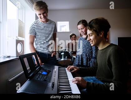 Geschwister schauen auf jungen Mann spielen Klavier Tastatur in hell Beleuchteter Raum Stockfoto