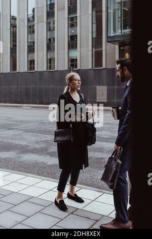 Unternehmerin mit Tasche im Gespräch mit Kollegin auf Bürgersteig in Stadt Stockfoto