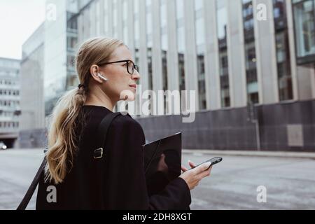 Rückansicht einer Geschäftsfrau mit in-Ear-Kopfhörern, in denen die Datei gespeichert ist Stadt Stockfoto