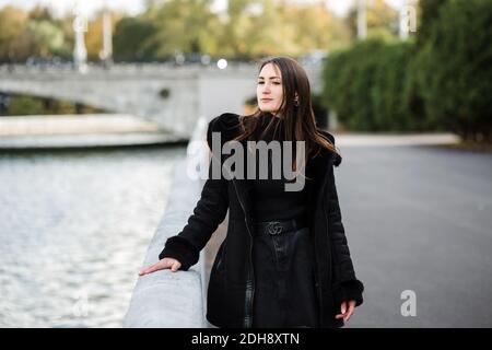 Ein Mädchen steht auf dem Damm in der Nähe des Wassers, in warmen Kleidern. Stockfoto