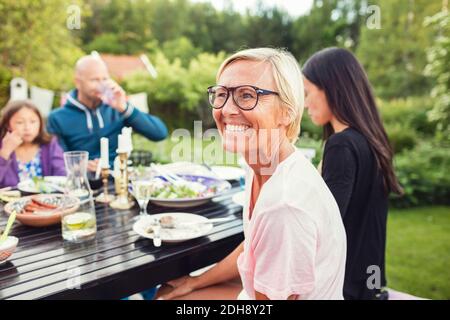 Glückliche Frau, die mit Freunden und Familie am Esstisch sitzt Im Hinterhof während Gartenparty Stockfoto