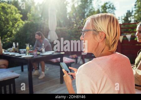 Rückansicht der glücklichen Frau mit Handy im Rücken Hof an sonnigen Tag Stockfoto